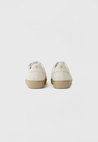 Off-white semsket sko med beige gummisåler, med minimal søm og logo detaljer på hælen, rund tå-design.