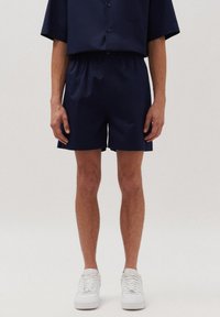 Marineblauwe shorts van lichtgewicht stof, met een elastische tailleband, zijzakken en een losvallende pasvorm. G gedragen met witte sneakers.