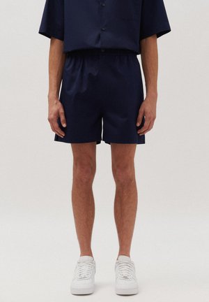 Marineblauwe shorts van lichtgewicht stof, met een elastische tailleband, zijzakken en een losvallende pasvorm. G gedragen met witte sneakers.