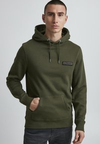 Olive green hoodie made of soft fabric, featuring a front pocket, drawstring hood, and a black label with "11 PROJECT" on the chest.