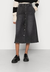 Zwarte denim midi rok met een sluiting aan de voorkant met knopen, riemlussen en zijzakken. Kenmerkt zich door een rechte snit en een lichte rafeling aan de zoom.