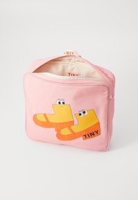 Rosa stoffpose med tegneserieaktige gule regnstøvler med blå øyne og en oransje stripe. "TINY" trykt i svart for ekstra detalj.