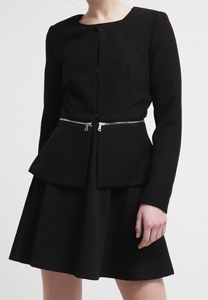 Schwarze Peplum-Jacke mit langen Ärmeln und rundem Ausschnitt, mit einem silbernen Reißverschluss-Akzent. Der Rock ist ausgestellt und aus strukturiertem Stoff.