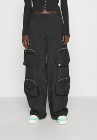 Zwarte cargo pants van lichtgewicht stof, voorzien van meerdere met rits afgesloten zakken en een ontspannen pasvorm. Gepaard met witte schoenen met groene accenten.