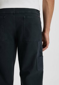 Mörkblå cargo byxor i kraftig bomullstyg, med stora sidofickor, förstärkt sömnad och en platt midja.