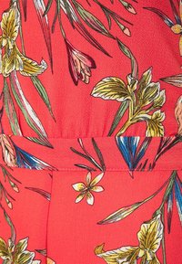 Tela roja con patrones florales en amarillo y rosa, decorada con hojas verdes. Superficie texturizada con acentos florales detallados, enfocándose en motivos naturales.