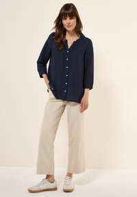 Camicia blu navy con bottoni in tessuto leggero, maniche a tre quarti. Abbinata a pantaloni larghi beige e sneakers bianche.