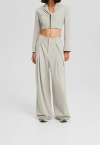 Blazer cropped grigio chiaro con zip e tasche frontali, abbinato a pantaloni a gamba larga con pieghe e vita alta.