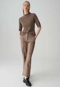 Bruine geribbelde gebreide trui met korte mouwen, gecombineerd met beige synthetische leren broek met gestructureerde naden, afgewerkt met zwarte schoenen.