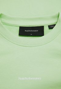 Lys grøn bomulds t-shirt med rund hals, med et sort label ved kraven og hvid logo tekst på forsiden. Størrelse M.