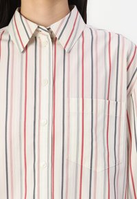 Collared button-up shirt made of lightweight fabric, featuring vertical stripes in red, navy, and cream, with a chest pocket on the left side.
