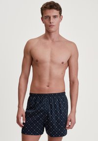 Marineblauwe boxershort met een geometrisch patroon in rood en wit. Elastische tailleband met knoopsluiting aan de voorkant; lichte stof.