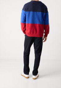Sudadera en bloques de color en azul marino, azul y rojo con puños acanalados. Combinada con pantalones negros y zapatillas blancas, con un acabado texturizado.