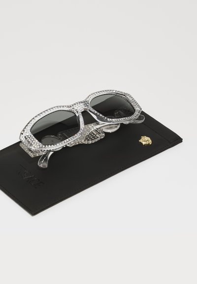 Black leather case with embossed logo, holding octagonal sunglasses featuring clear rhinestone accents and dark lenses.