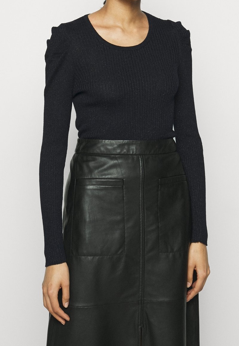 Marineblaues, geripptes Langarmoberteil mit puffigen Schultern, kombiniert mit einem schwarzen Lederrock mit Vordertaschen und einem zentralen Reißverschlussdetail.