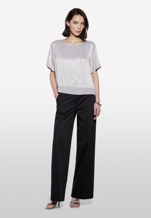 Top in raso grigio chiaro con maniche corte e scollatura arrotondata, abbinato a pantaloni neri a vita alta e sandali con tacco argento.