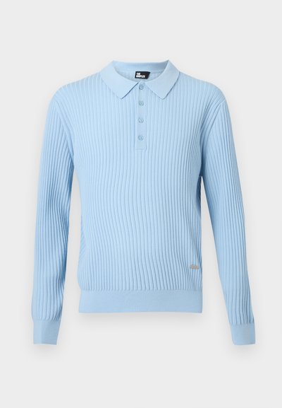 Polo à manches longues côtelé bleu clair avec patte de boutonnage et petite étiquette en métal de la marque sur le côté avant inférieur.