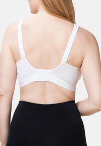 Reggiseno sportivo bianco con schiena in rete testurizzata, spalline regolabili e chiusura con gancetto. Abbinato a leggings neri a vita alta.