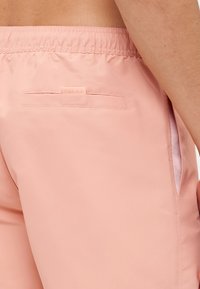Roze, lagane kratke hlače s elastičnim pojasom, s stražnjim džepom i bočnim detaljima, izrađene od glatkog, vodoodpornog materijala.