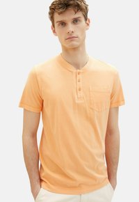 Kortærmet, lyseorange henley-shirt med knaplukning, brystlomme og blød tekstur; enkelt design med en afslappet pasform.