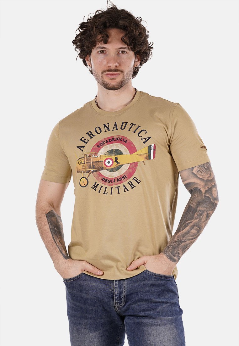 T-shirt beige con una grafica rotonda che raffigura un aereo e il testo "Aeronautica Militare." Maniche corte, design aderente, tessuto in cotone.