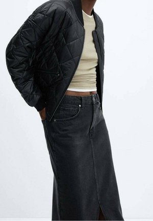 Person iført en sort quiltet bomberjakke, beige cropped top og et høj-taljet sort denimskørt med frontslids.