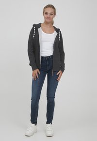 Šedá mikina na zips s bielymi šnúrkami, nosená na bielom tielku. V kombinácii s tmavými džínsami skinny a bielymi teniskami.