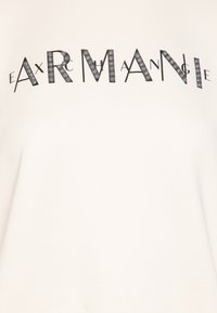 Sudadera de color beige claro con un logo gráfico negro "ARMA" adornado con strass y una textura suave.
