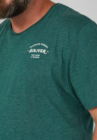 Teal crewneck t-shirt gemaakt van zachte stof. Heeft een witte afgedrukte logo op de borst met de tekst "S. OLIVER" en "ELEVATED CASUAL."