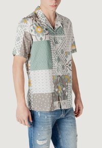 Camisa de manga corta con un diseño de patchwork que presenta patrones florales y geométricos en tonos suaves de verde, naranja y gris.