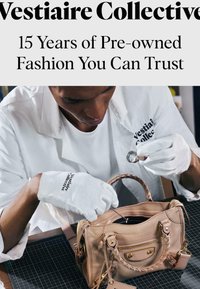 Personne portant des gants blancs et un manteau blanc inspecte un sac à main en cuir beige avec une loupe sur une table de travail.