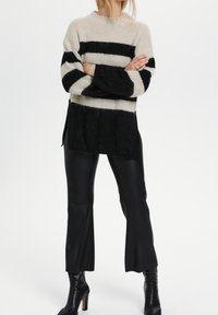 Neulepaita, jossa on kerma- ja mustat raidat, korkea kaulus, yhdistettynä mustiin tekonahkahousuihin ja nilkkapituiset mustat korkokengät.