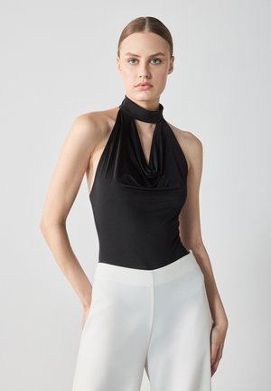 Black halter neck bodysuit in smooth fabric with draped front, paired with high-waisted white trousers featuring a minimalist design and wide legs.