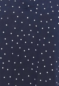 Haut en tissu bleu marine avec un design à col en V, orné de pois blancs de tailles variées répartis uniformément sur le matériau.
