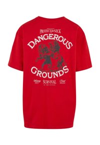 Rød bomulds t-shirt med grafisk print af to løver, med tekstene "DANGEROUS GROUNDS" og "SURVIVAL OF THE FITTEST" i hvid.