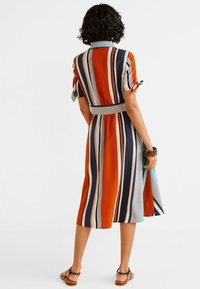 Robe rayée aux couleurs orange, bleu marine et crème. Manches courtes avec liens, taille ceinturée et ourlet arrivant au genou. Tissu en coton ou similaire.