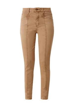 Beige fitted broek met stikseldetails aan de zijkant, gecombineerd met een witte blouse met lange mouwen en gestreepte sneakers. Neutrale achtergrond.