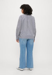Striped blouse in navy and white, relaxed fit, long sleeves, with a curved hem; paired with light blue wide-leg jeans and silver shoes.