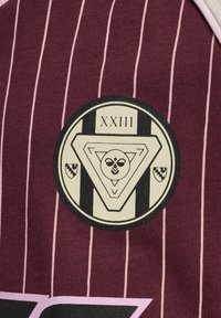 Bordeaux stof med lodrette lyserøde striber, prydet med et rundt logo med en trekant og dekorative elementer i sort og creme.