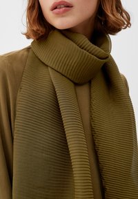 Écharpe texturée vert olive avec un motif en relief, drapée lâchement sur un vêtement de couleur similaire. Tissu lisse avec un éclat subtil.