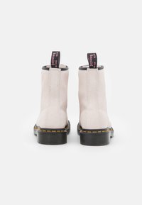 Stivali ankle in suede beige chiaro con suole in gomma nere, cuciture gialle e passanti rosa a contrasto sul retro.