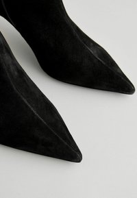 Scarpe nere in suede con tacco alto, punta affusolata e texture liscia. Presentano un profilo elegante e dettagli di cucitura visibili.