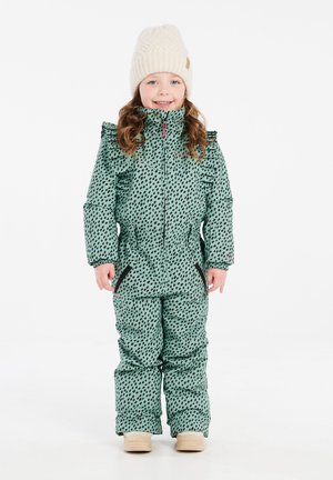 Tuta da neve verde a fantasia con macchie nere, caratterizzato da un collo alto e rouches, abbinato a un cappello in maglia color crema e stivali beige.