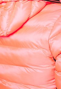 Jasnoróżowa pikowana kurtka puchowa w kolorze koralowym z poziomym przeszyciem i czarnym zamkiem błyskawicznym widocznym na górnej krawędzi.