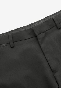 Pantalones de vestir gris oscuro con una textura suave, que cuentan con presillas para cinturón, frente plano y costuras limpias a lo largo de las asas.