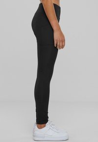 Leggings neri con una vita alta, caratterizzati da un design elegante e una superficie liscia, abbinati a scarpe da ginnastica bianche.