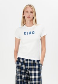 Hvit bomulls t-skjorte med blå, lodden "CIAO" skrift på forsiden, kombinert med blå og svart rutete bukser.