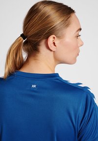 Blå sportsjersey lavet af et glat materiale, med hvide accenter på skuldrene og "XK"-logoet ved nakken bagpå.