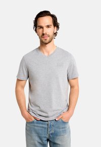 Sivé bavlnené tričko s výstrihom do V, krátkymi rukávmi a jemným vyrazeným logom na hrudi, doplnené svetlomodrými denimovými džínsami.
