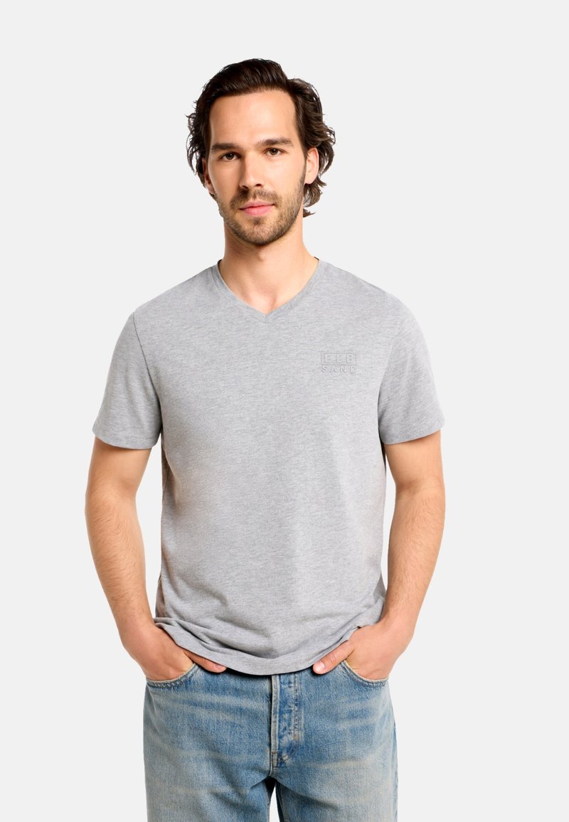 Sivé bavlnené tričko s výstrihom do V, krátkymi rukávmi a jemným vyrazeným logom na hrudi, doplnené svetlomodrými denimovými džínsami.